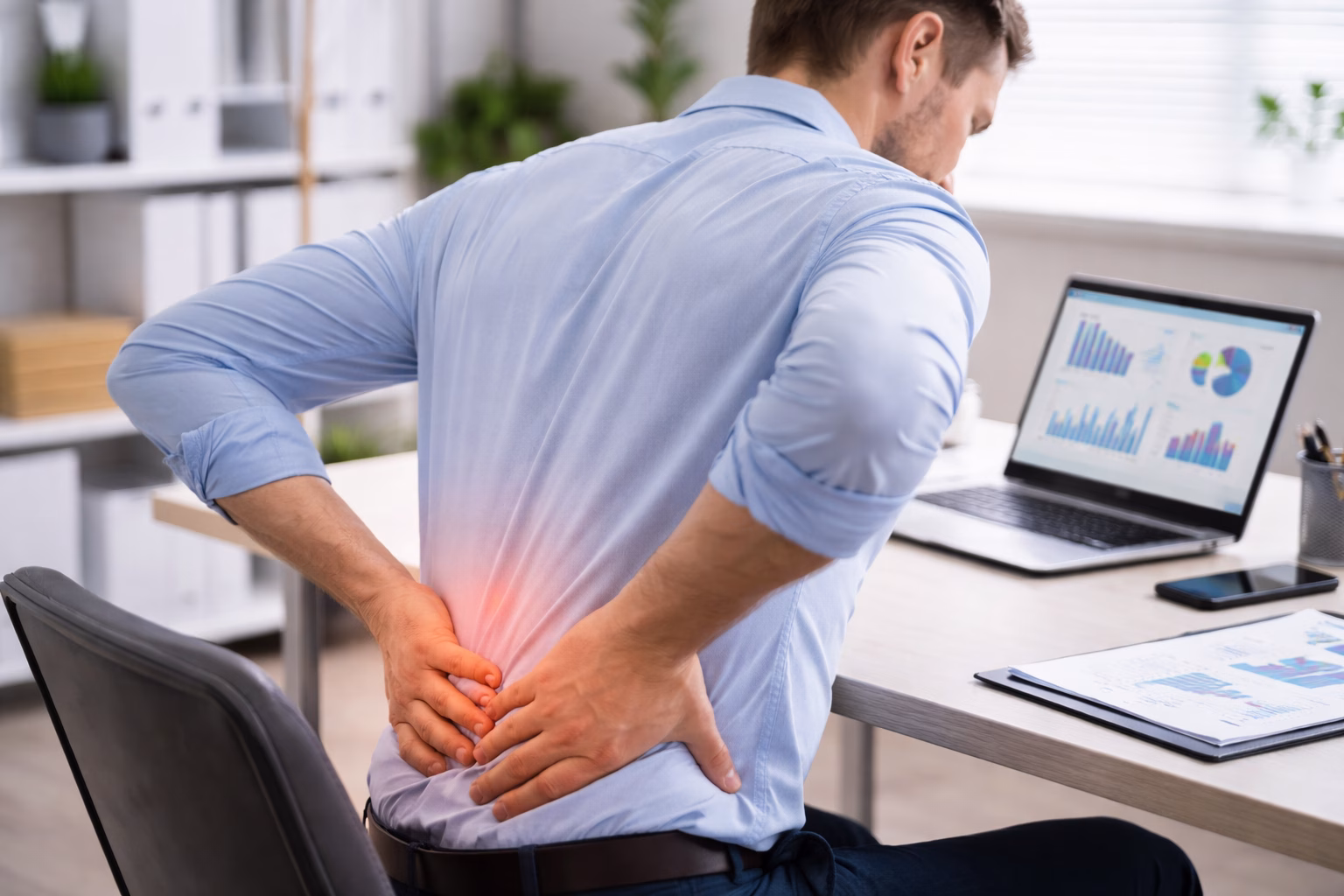 Office worker holding lower back while sitting on chair at office